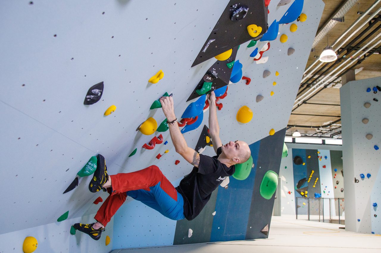 Mann klettert in Linz in der Boulderhalle fokussiert auf den naechsten Griff