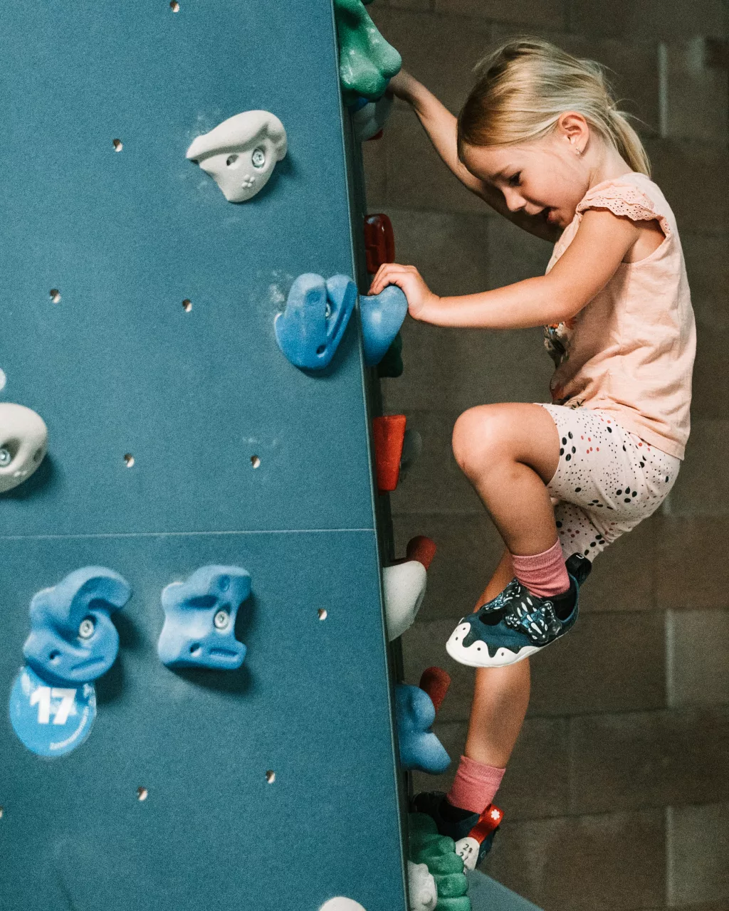 Mädchen beim Indoor-Klettern an einer bunten Kletterwand.