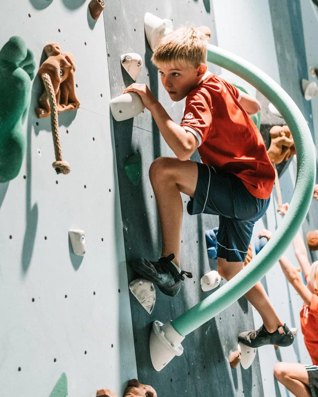 Junger Junge beim Klettern an einer Indoor-Kletterwand mit verschiedenen Hindernissen.